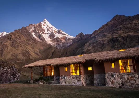Stone building with a straw roof in the middle of a grass valley, with large mountains in the background