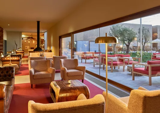 Indoor lounge area with cushioned chairs and large windows showing an outdoor patio