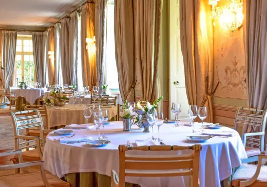 Dining area with large curtains, circular tables, and wine glasses on each table