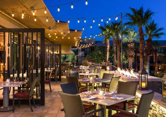 Outdoor dining area with string lights and palm trees to the right