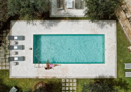 Man and woman laying down in an outdoor pool with gray pool chairs on the left