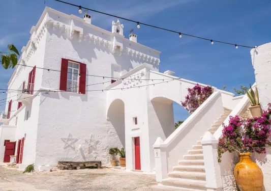 White stone building with red windows and doors, with a stairway on the right