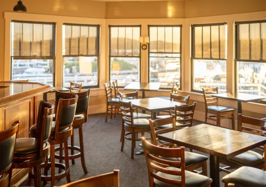Indoor dining area surrounded by windows, looking out towards a harbor
