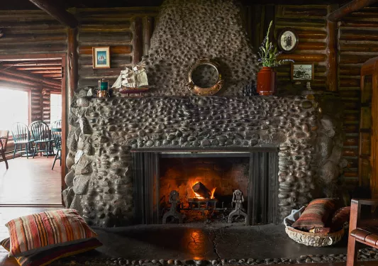 Fireplace made of stone, with a dining area to the left in a separate room