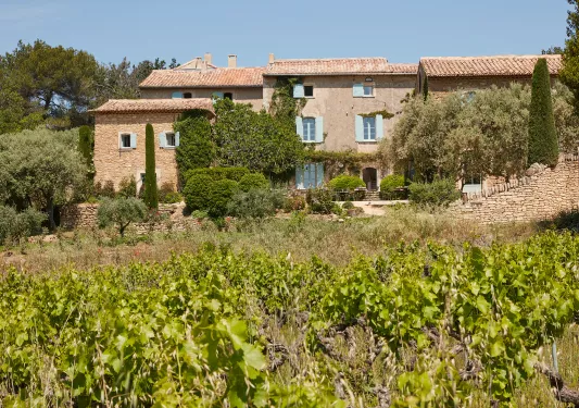Red-brick building with green crops and trees in front