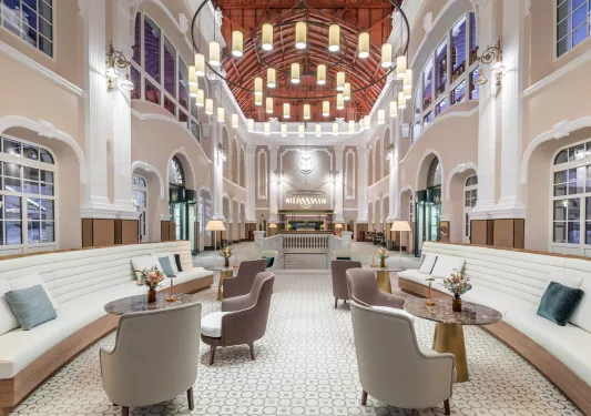 Large, wide hall with white and tan cushioned chairs and a large, circular light fixture in the center