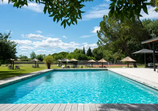 Outdoor pool surrounded by umbrellas and a grass field