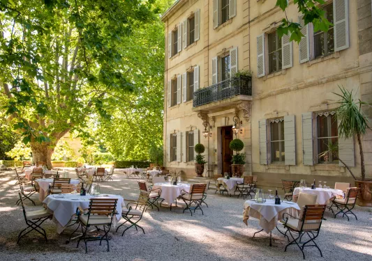 Outdoor dining area with circular tables next to a rustic, yellow building