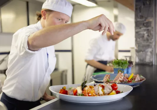 Chef preparing a plate of food, including kabobs and salads