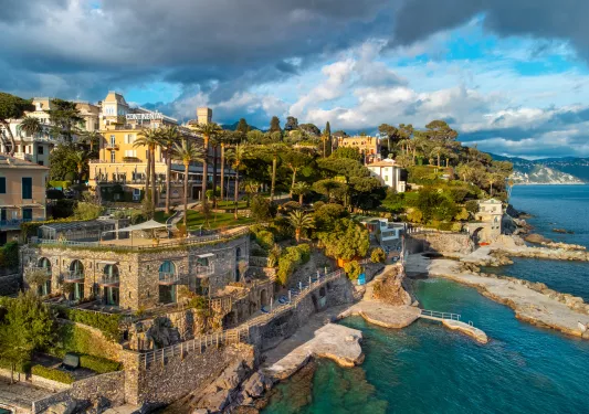Exterior view of a stone building next to the ocean, with tall trees in the background
