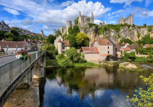 Bridge over a river with large, rustic ruins in the background