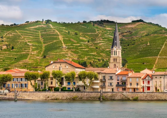 Tan buildings next to a lake, with grassy hills in the background