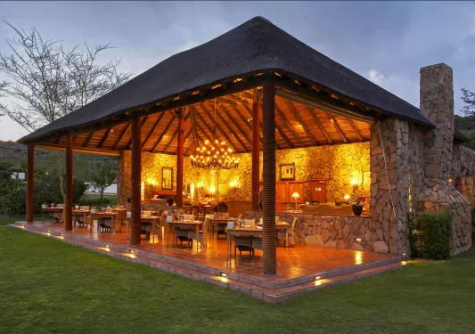 Outdoor, open dining patio with a chandelier, surrounded by a grassy area