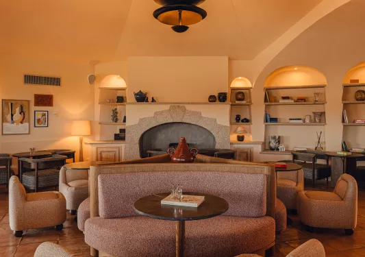 Indoor lounge with cushioned sofas, circular tables and a fireplace in the background