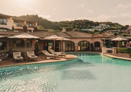 Outdoor pool with white, reclined chairs and white umbrellas surrounding
