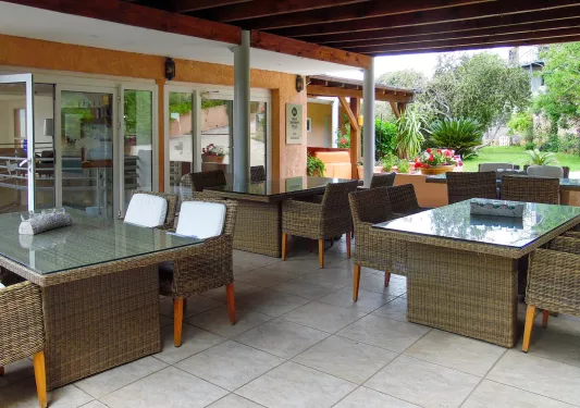 Ourdoor dining area with woven chairs and tables, under an outdoor patio