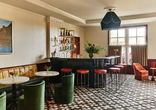Indoor bar and lounge, with green cushioned chairs and red bar stools