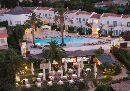 Sky view of white and tan buildings with an outdoor pool and tall palm trees