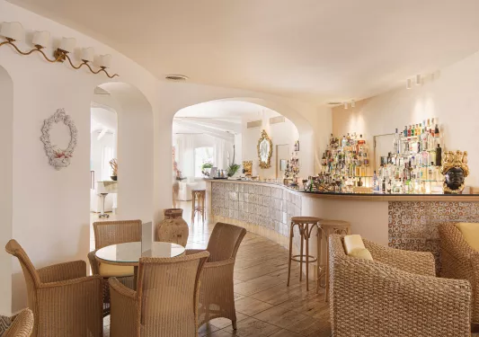 Bar and lounge with white walls, tiles on the bar, and woven chars around each table