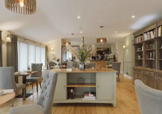 Indoor dining tables with wine glasses and a wooden counter with a vase in the center