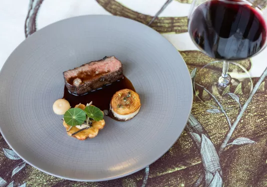 Gray plate with meat small pieces of meat and potatoes, next to a glass of wine