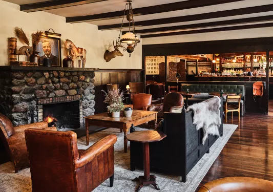 Lobby with leather couches in front of a fire place, with a bar in the back right
