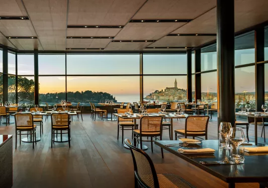 A hotel dining room with many tables and large windows overlooking the water