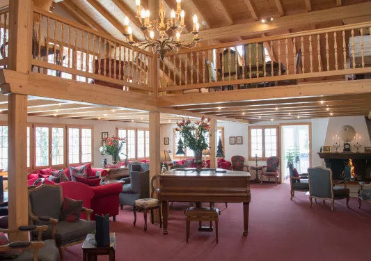 Wooden cabin lounge with red and gray chairs, with a wooden piano in the center
