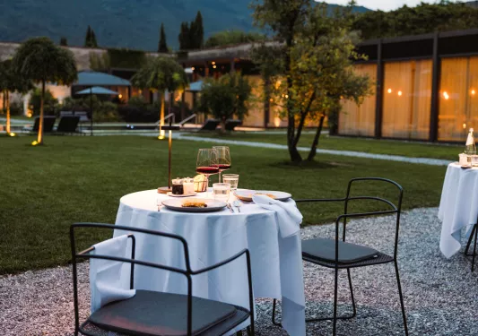 Outdoor dining table with a white cloth and two plates of food and two glasses of wine