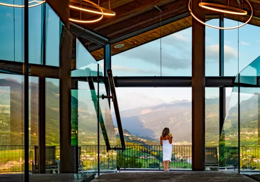 Woman wrapped in a white towel looking at a grassy, mountain