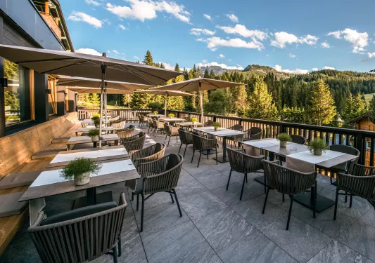 Outdoor dining area with woven, brown chairs, looking out to a valley of trees