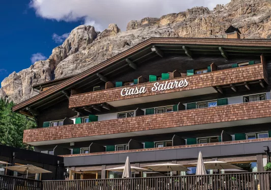 Exterior view of hotel building with wooden balconies and a mountain in the background