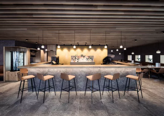 Bar in the center of a lounge, surrounded by wooden stools