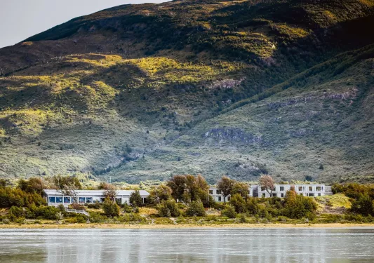 Long white hotel building surrounded by trees and a large hill