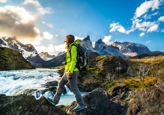 Person in green jacket crossing through rocks with a river in the background