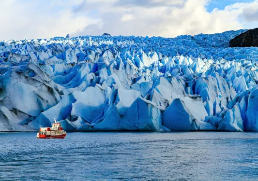 Jagged snow caps with a red and white boat traveling in front