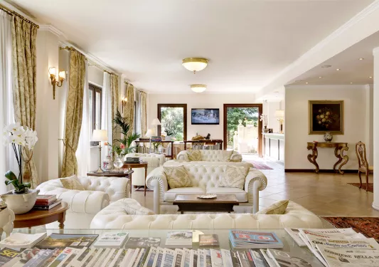 Indoor lobby with white, cushioned chairs and open doors leading to an outdoor garden