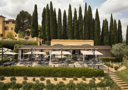 Outdoor garden and patio, with trimmed bushes and black chairs and tables
