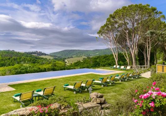 Outdoor infinity pool surrounded by green and red reclining chairs with a view of mountains in the distance