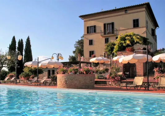 Outdoor pool in front of a hotel building, surrounded by umbrellas