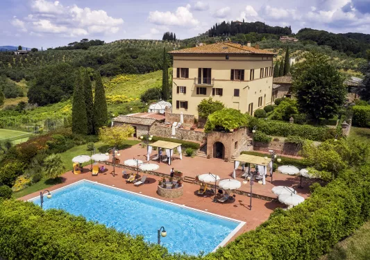Hotel building with an outdoor pool and lounge, surrounded by trees and green plants