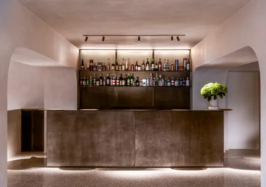 Gray bar counter with liquor on a shelf on the wall, illuminated by lights