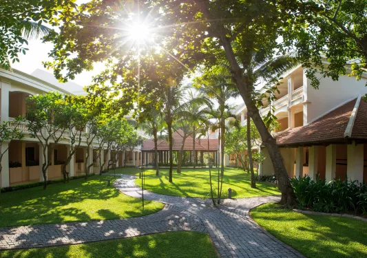 Outdoor courtyard between two white buildings, with a grass field and small palm trees