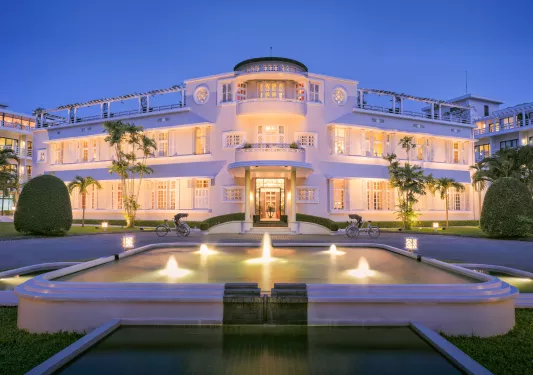 Exterior view of illuminated white building with an illuminated fountain in front