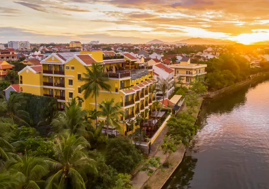 Sky view of yellow hotel building with a lake to the right and the sunset in the background