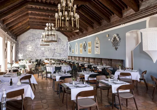 Large dining hall with tables and wooden chairs, with three large candle chandeliers