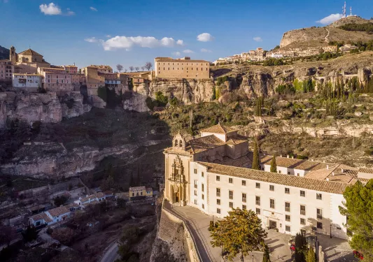 Rustic, cathedral-like buildings on a cliff, with smaller houses on the ground level