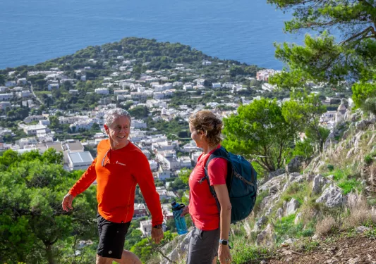 Man and woman walking on a dirt trail on a hill, with a town in the distance