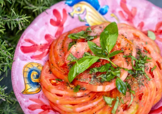 A pink plate, full of sliced tomatoes and parsley on top