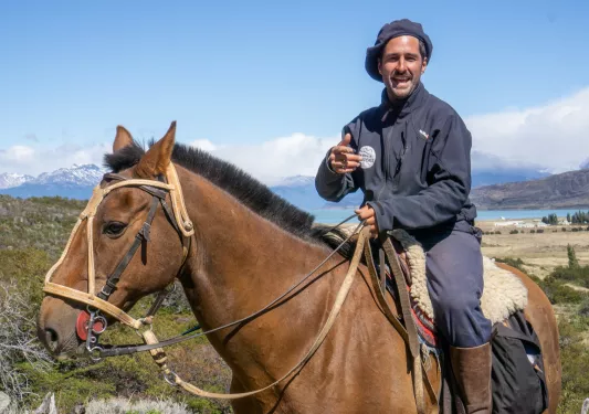 Man smiling, while riding a horse and pointing at the camera